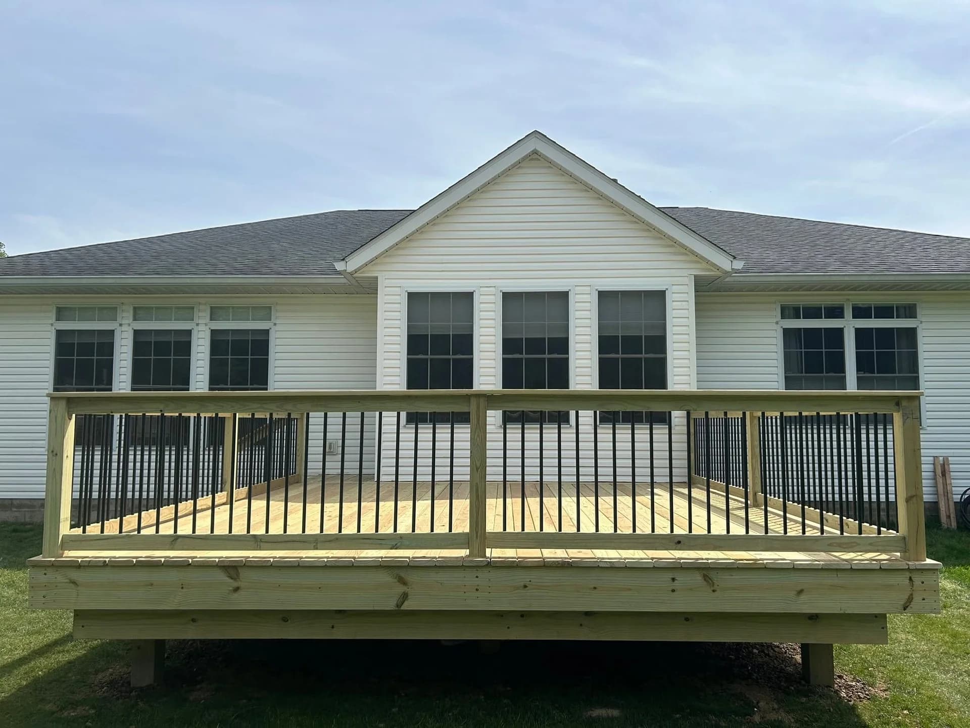 Completed pressure-treated wood deck with black metal balusters behind a white house
